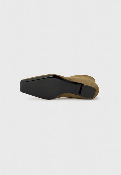 Zapato de tacón alto de ante marrón con punta afilada y suela de goma negra. Presenta una textura suave y un tacón contorneado y afilado.