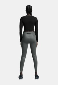 Schwarzes langärmliges Crop-Top kombiniert mit enganliegenden grauen Leggings mit Gesäßtaschen und strukturierten Details; sportliches Design mit funktionalen Akzenten.