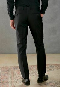 Schwarze maßgeschneiderte Hose mit glatter Textur, im Slim-Fit, mit Gesäßtaschen und dezenten Streifen, kombiniert mit schwarzen Schuhen.