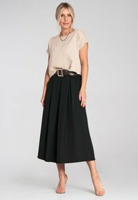 Beige strukturierter Oberteil mit kurzen Ärmeln, kombiniert mit einem schwarzen Faltenrock. Brauner Gürtel mit einer großen Schnalle. Helle Riemchen-Heels.