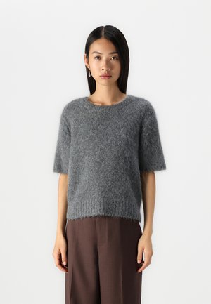 Gray, short-sleeve knit sweater made from fluffy material with a round neckline and ribbed hem, worn with brown trousers.