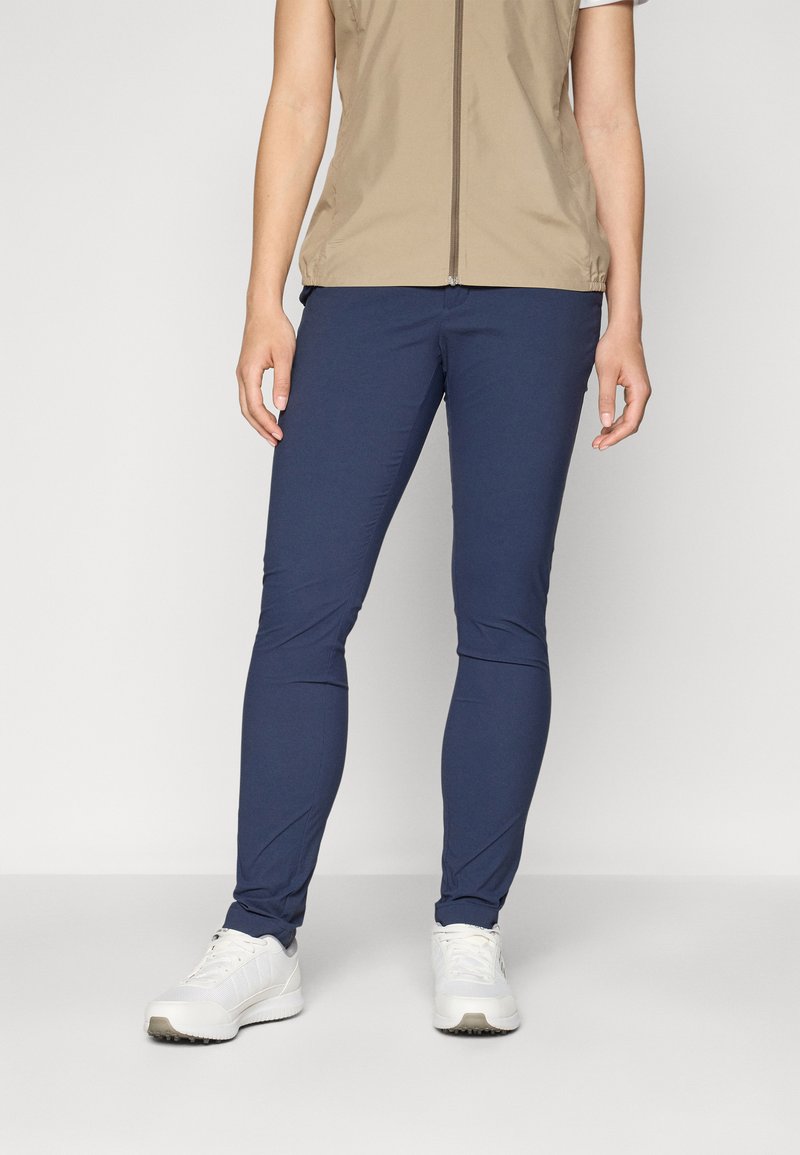 Navy blue stretch pants with a smooth texture, slim fit, and elastic waistband. Paired with white athletic shoes.