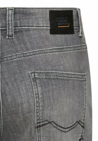 Achterzak van een grijze spijkerbroek met zwart-oranje "camel active" merklabel vlakbij de tailleband.