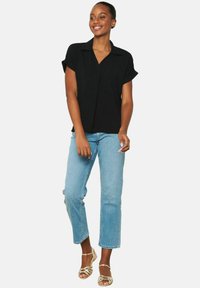 Camicetta nera a maniche corte con colletto, abbinata a jeans dritti blu chiaro e sandali dorati. Il tessuto sembra liscio e ha una vestibilità comoda.