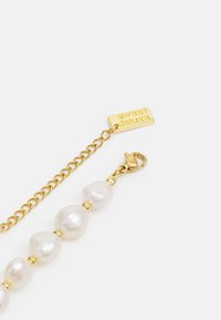 Guldarmband med oregelbundet formade vita pärlor och guld detaljer, med karbinlås och inpräntad tag.