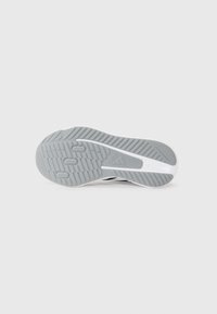 Semelle de chaussure de sport en gris avec un motif de grip texturé, présentant un accent blanc sur le côté et de profondes rainures pour l'adhérence.
