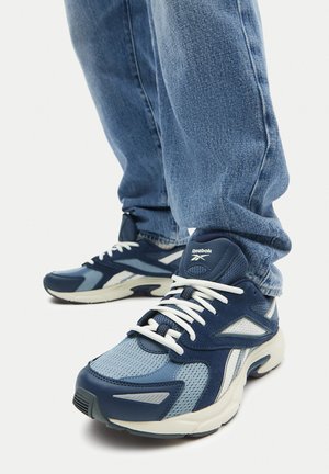 Zapatillas deportivas azules que combinan materiales de malla y cuero, con cordones blancos, acentos texturizados y un diseño de suela intermedia gruesa.