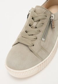 Basket en daim gris clair avec des lacets tressés, fermeture éclair latérale et semelle en caoutchouc texturé. Présente des coutures discrètes et une finition lisse.
