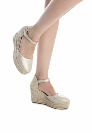 Sandalias de cuña beige con un acabado metálico, plataforma de yute tejido y correa al tobillo. Superficie suave con detalle texturizado en el tacón.