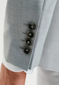 Jasnoszara marynarka w stylu garniturowym z teksturowanej tkaniny, z czterema ciemnymi guzikami na mankietach, uzupełniona ozdobnym przeszyciem.
