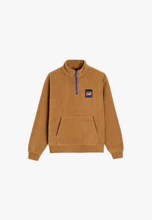 Brązowy polarowy pulower z półzamkiem przy kołnierzu, przednią kieszenią i niebieskim zamkiem błyskawicznym. Ma naszywkę z logo na lewej piersiach. Miękka faktura.