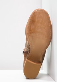 Brązowy but teksturowany z suwakiem i płaską podeszwą. Spód ma gładkie wykończenie oraz wytłoczone logo motyla.