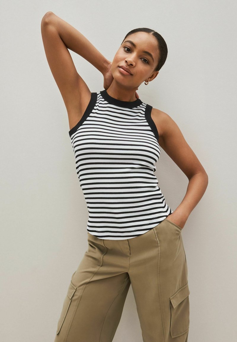 Black and white striped sleeveless top with a high neck and contrasting black trim, paired with khaki cargo pants featuring side pockets.