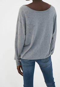 Grijze lange mouwen pullover met een brede halslijn, versierd met sterpatronen met embellishments op de rug, gecombineerd met blauwe jeans.