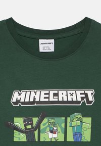 Grön bomullströja med en Minecraft-logotyp och tre pixelerade karaktärsillustrationer på framsidan. Rund halsringning, korta ärmar.