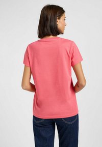T-shirt à manches courtes, col rond en tissu de coton corail, offrant une coupe décontractée et une texture lisse. Porté avec un jean en denim foncé.