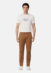 T-shirt in cotone bianco con stampa grafica blu, abbinata a chinos marroni e sneaker bianche. Design semplice e aderente con trame morbide.