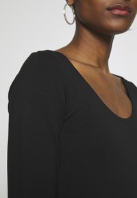 Czarny top z długim rękawem i okrągłym dekoltem, wykonany z miękkiej, teksturowanej tkaniny. Posiada dopasowany krój i czysty, minimalistyczny design.
