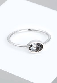 Bague en argent ornée d'une pierre précieuse ovale grise, avec un anneau lisse et une finition polie. La pierre est facettée, ce qui améliore sa qualité réfléchissante.