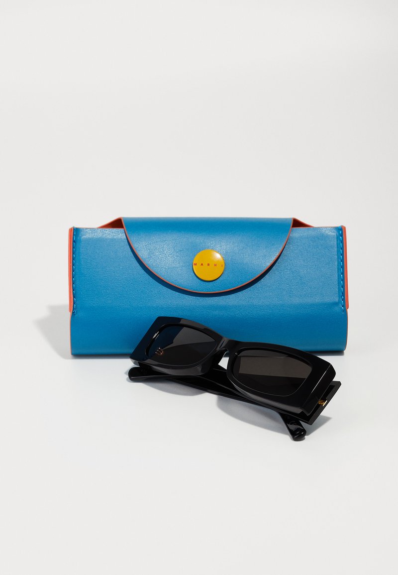 Étui à lunettes en cuir bleu avec des accents orange et un bouton jaune, accompagné de lunettes de soleil rectangulaires noires avec des verres teintés.