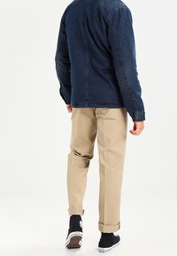 Džínová bunda tmavě modré barvy, světle hnědé chino kalhoty a černé tenisky. Oblečení má volný střih s ohrnutými lemy na kalhotách.