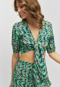 Cropped top floreale verde con maniche a sbuffo e dettaglio annodato sul davanti, abbinato a una gonna coordinata con un motivo simile.