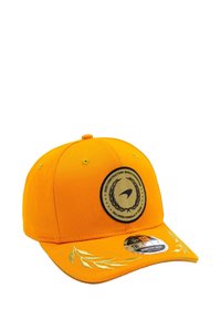 Pomarańczowa czapka z daszkiem z okrągłym czarnym emblematem zdobionym złotymi detalami i wzorem laurowym na daszku. Wykonana z bawełnianej tkaniny, o usztywnionej konstrukcji.
