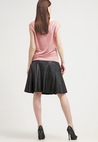 Růžový top s krátkým rukávem a krajkovými detaily na ramenou, kombinovaný s černou koženou sukní ve tvaru A. Celkový vzhled doplňují černé vysoké podpatky.