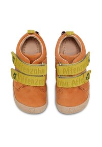 Oranje corduroy schoenen met twee gele klittenbandsluitingen met geprinte tekst, ronde neus en rubberen zool met subtiele textuur.