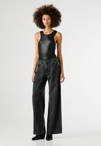 Melna sieta bez piedurknēm, kas kombinēta ar platām melnām džinsām, kurām ir sudraba kniedes, un ar punktetām melnām potīšu zābakiem.