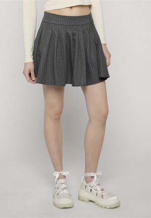 Mujer con falda plisada gris a rayas, top corto crema de manga larga y zapatos plataforma blancos con cordones de cinta blanca.