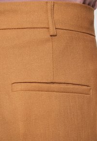 Tissu texturé orange de pantalons bien tailleur avec une poche arrière, fini propre et détails de couture subtils.