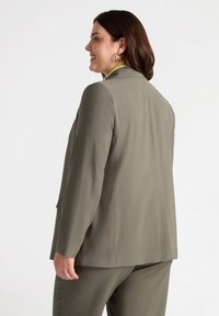 Sacou verde măsliniu cu croială ajustată, închidere cu un buton și textură netedă. Prezintă un guler jos și două buzunare laterale.