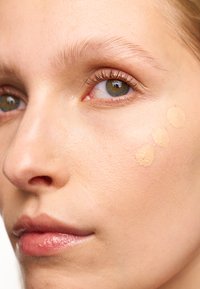 Foundation swatches in three circular dots on a light skin tone, against smooth skin with natural tint, near eyes with subtle lashes.