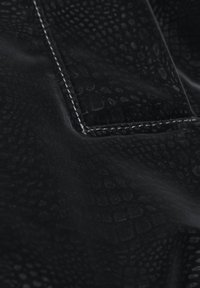 Mustast kangast, millel on peen reljeefne roomajamuster ja nähtavad valged õmblused, mis joonistavad taskunurga kontuuri.