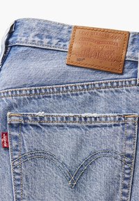 Ljusblå denimjeans med en brun läderlapp med präglad text och en signatur röd etikett på bakfickan.