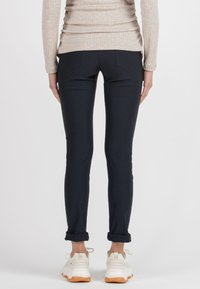 Navy blue fitted pants with a smooth texture, two back pockets, and rolled cuffs, paired with white sneakers featuring orange accents.