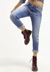 Světlé modré džíny z denimu s ohrnutými lemy, doplněné vínovými kotníkovými botami na šněrování. Džíny mají přední zapínání na knoflík a zip.