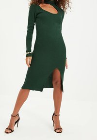 Robe à manches longues côtelée en vert foncé avec un décolleté en trou de serrure et une fente sur le côté, présentant une silhouette ajustée et un tissu texturé.
