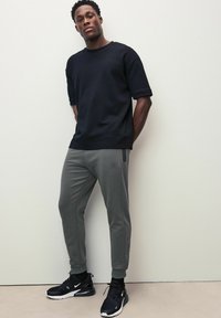 Schwarzes Kurzarm-Sweatshirt, graue tapered Jogginghosen mit Taschen und schwarze Sportschuhe mit weißen Akzenten. Glatter Stoff, lässige Passform.