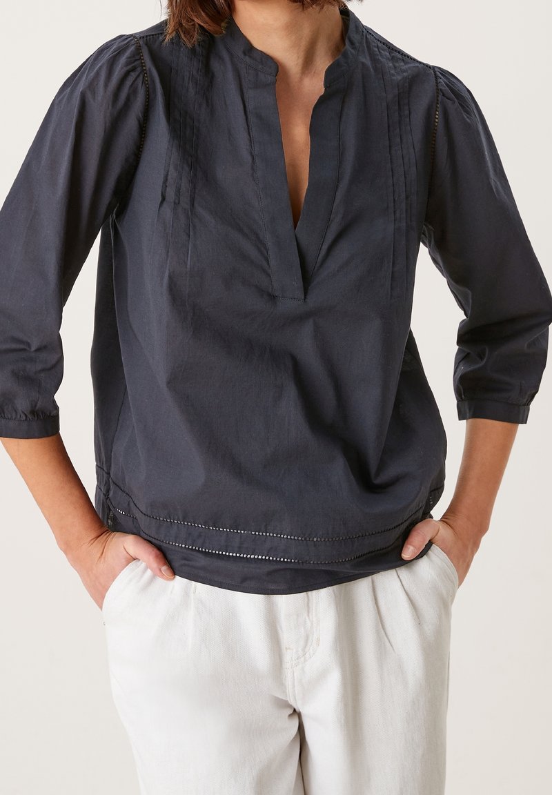 Blouse en coton bleu marine avec un col en V, des manches trois-quarts et des plis Tucks ; présente une couture subtile sur l'ourlet du bas.