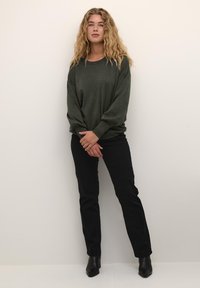 Maglione a maglia verde oliva con maniche lunghe, vestibilità normale; abbinato a jeans neri aderenti e stivaletti neri con tacco. Texture liscia, design semplice.
