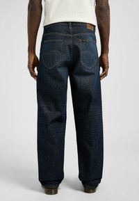 Dark blue denim jeans with a loose fit, featuring a waistband label, two back pockets, and a straight leg design.