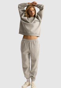 Szara, krótka bluza z długim rękawem i dopasowane dresowe spodnie z miękkiego materiału. Posiada elastyczny pas i mankiety, a także luźny krój.