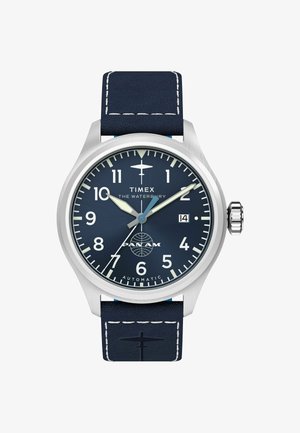 Timex Waterbury avtomatska ura z mornarsko modrim številčnikom, belimi številkami, logotipom letala, oknom za datum in mornarsko usnjeno zapestnico z belim šivom.