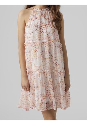 Robe blanche sans manches avec un motif à petits pois multicolores, des volants superposés et un col haut froncé, portée par une personne debout.