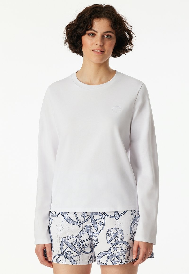 Vit långärmad skjorta med rund halsringning och en subtil broderad logotyp. Bärs med mönstrade shorts med blå och vita mönster.