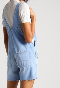 Lichtblauwe denim overall met een relaxte pasvorm, voorzien van twee achterzakken, knoopsluitingen en rafelige randen bij de shortzoom.