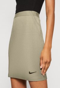 Oliwkowa, prążkowana spódnica o dopasowanym fasonie, z niewidocznym pasem i małym czarnym logo Nike na dolnej krawędzi.