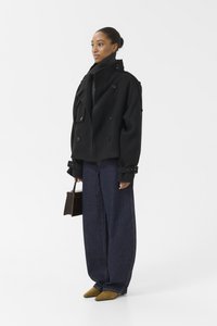 Zwarte dubbelrijige wollen blend peacoat met epauletten, gecombineerd met wijde spijkerbroek en mosterdgele puntige schoenen, met een donkerbruine handtas.